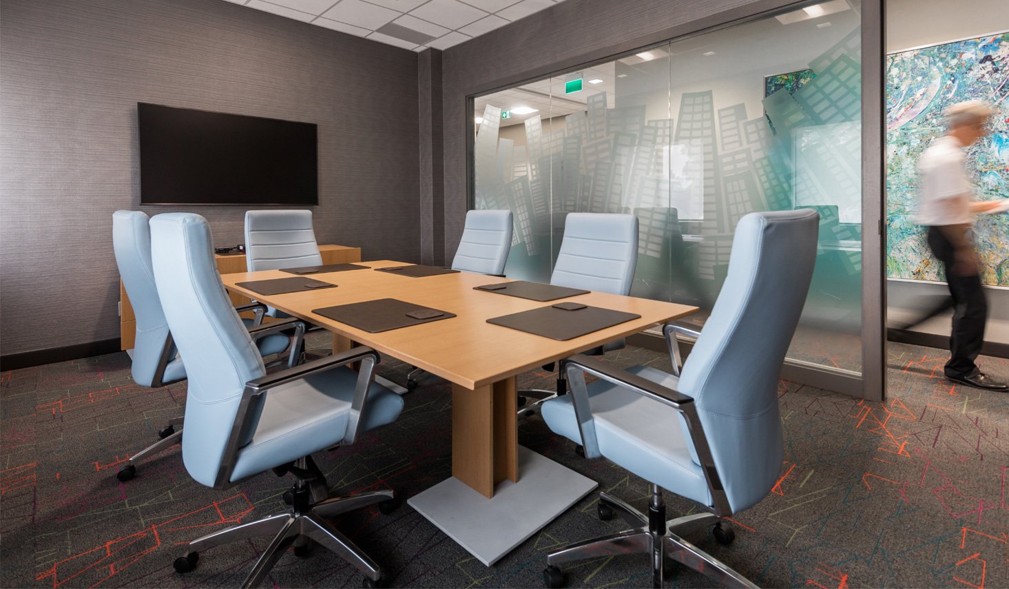 Modern Acorn Developments boardroom with light blue chairs, a wood conference table and a frosted glass wall etched with a city skyline